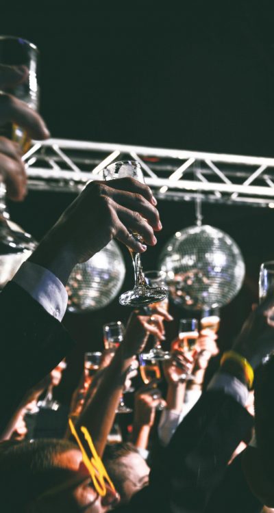 A festive gathering with people raising glasses in a toast under shiny disco balls at a night event.