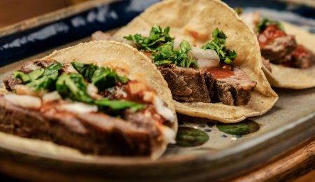 Three mouth-watering Mexican tacos served on a platter with fresh cilantro and onions.